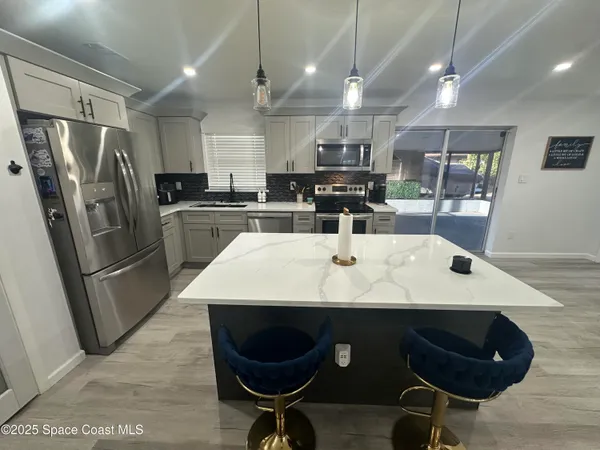 a kitchen with stainless steel appliances kitchen island granite countertop a sink a stove a refrigerator cabinets and chairs