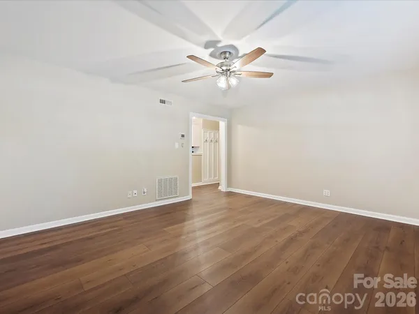 an empty room with wooden floor fan and windows