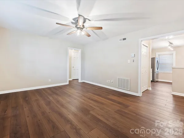 a view of an empty room with wooden floor and a ceiling fan