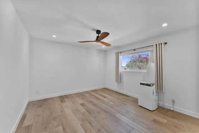 a view of an empty room with wooden floor and a ceiling fan