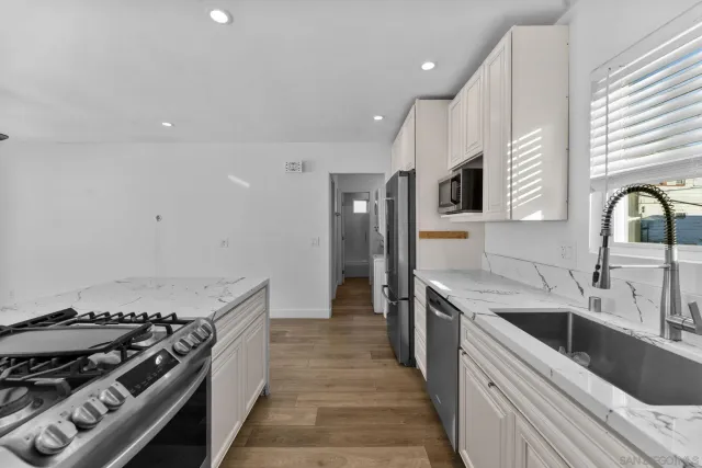 a kitchen with stainless steel appliances a sink dishwasher a stove top oven a refrigerator with wooden floor and cabinets