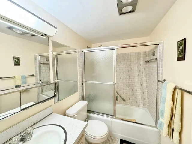 a bathroom with a granite countertop bathtub shower sink mirror and toilet