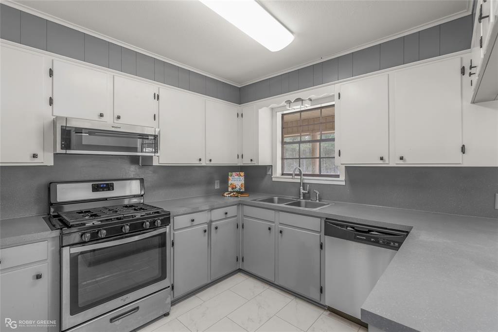 1303 Young Road Benton, LA 71006 - Photo 13 of 34 Kitchen with stainless steel appliances, crown molding, white cabinetry, light marble finish flooring, and light countertops