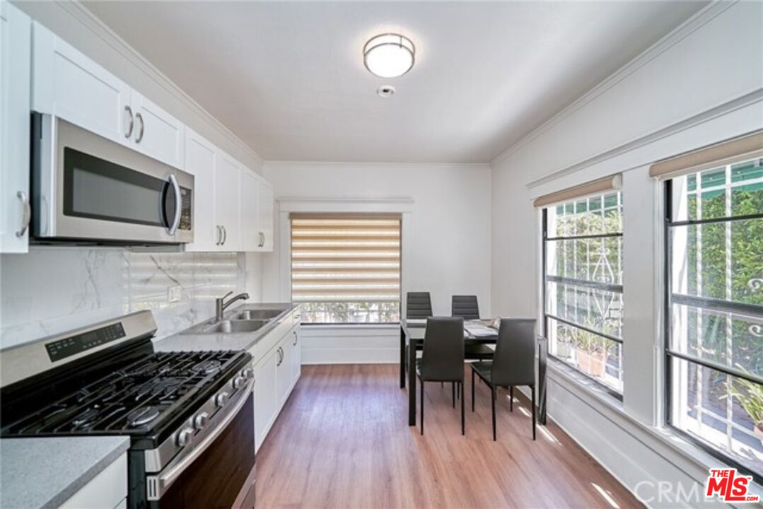 1023 South Wilton Place Los Angeles, CA 90019 - Photo 15 of 34 a kitchen with stainless steel appliances a stove a sink dishwasher a dining table and chairs with wooden floor
