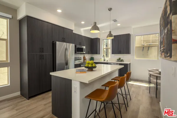 a kitchen with stainless steel appliances a dining table chairs refrigerator and microwave