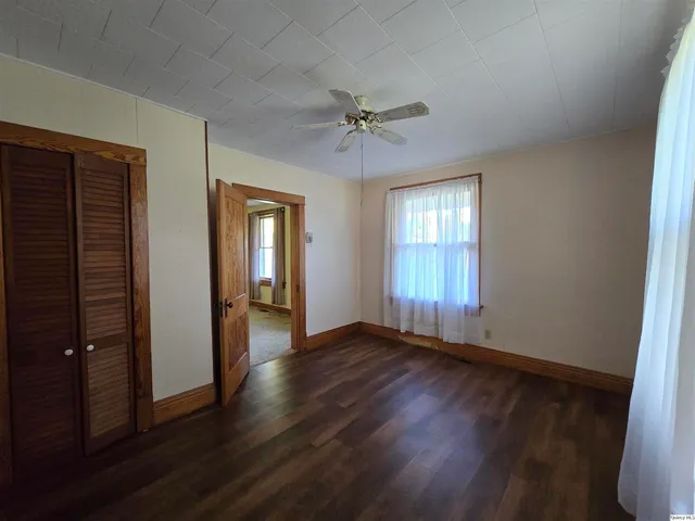 an empty room with wooden floor fan and windows