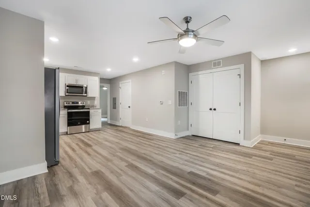 a view of an empty room with wooden floor and a ceiling fan