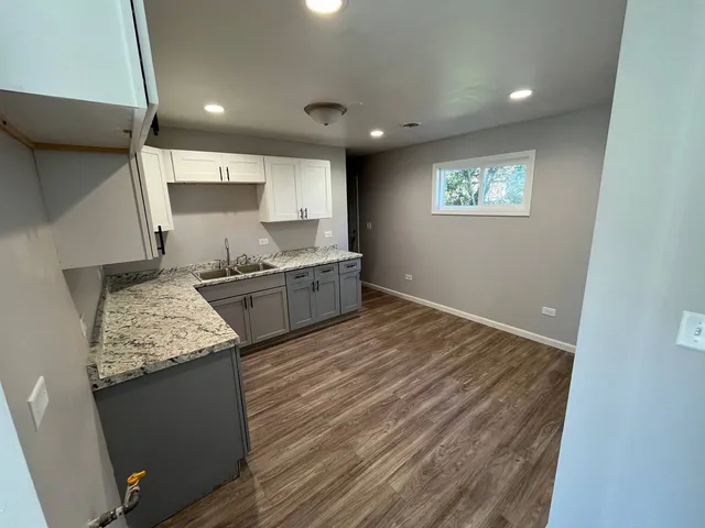 a room with kitchen island granite countertop wooden floors and a sink