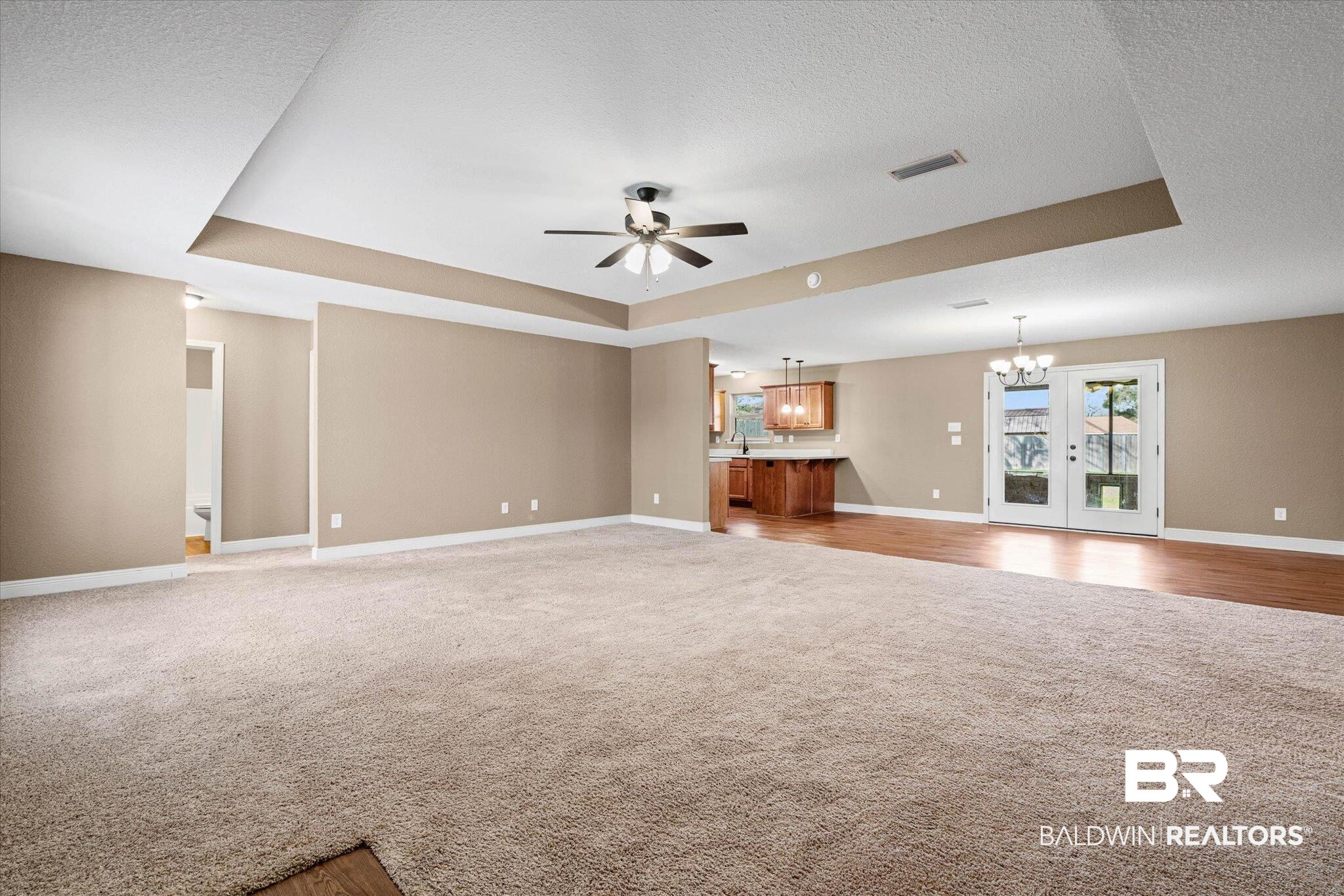 101 Washington Boulevard Foley, AL 36535 - Photo 2 of 32 Unfurnished living room with a tray ceiling, suspended lighting, ceiling fan, light carpet, and a textured ceiling