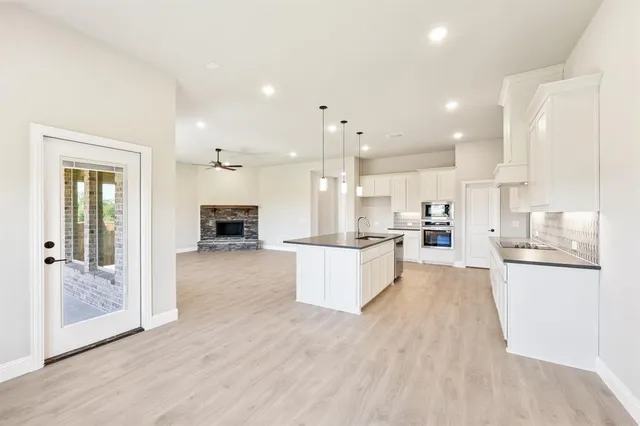 a large white kitchen with kitchen island a stove a refrigerator a sink and white cabinets with wooden floor
