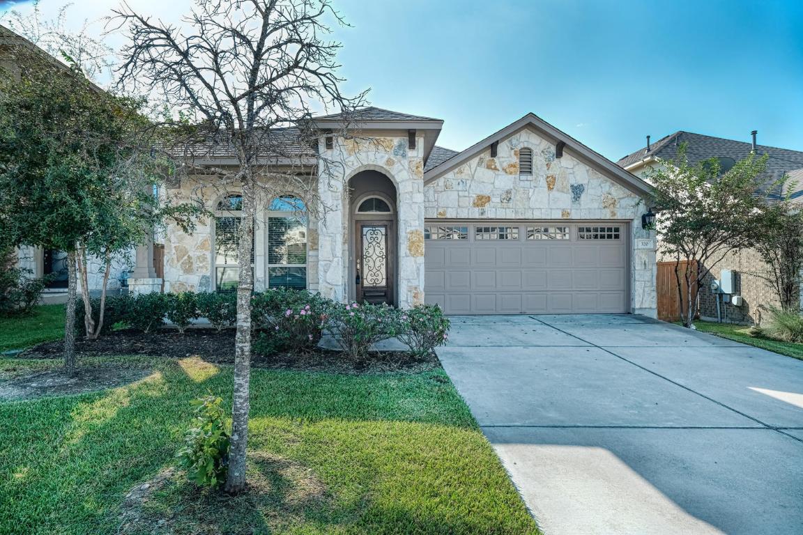 French provincial home featuring stone siding, driveway, an attached garage, and a front yard