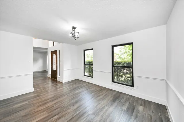 an empty room with wooden floor chandelier and windows