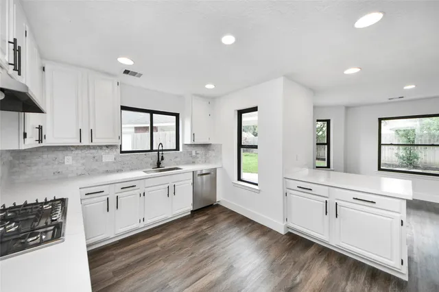 a large white kitchen with granite countertop a stove a sink a refrigerator and white cabinets with wooden floor