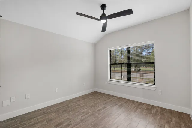 an empty room with wooden floor ceiling fan and windows