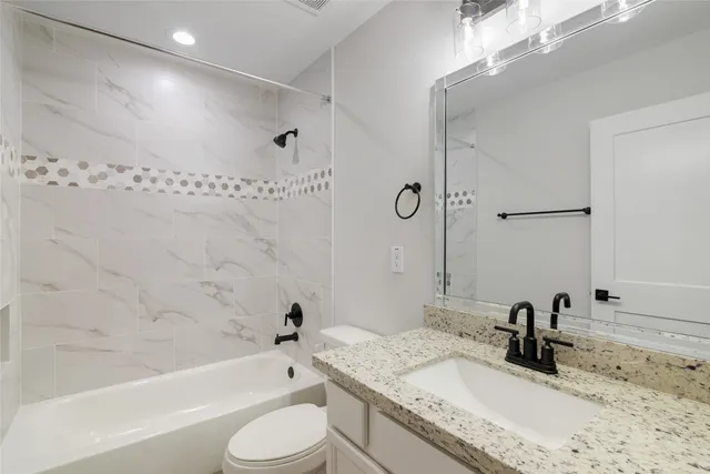 a bathroom with a granite countertop bathtub sink vanity mirror and toilet