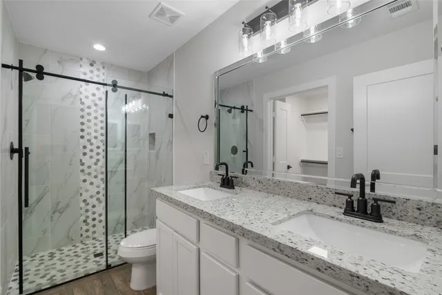 a bathroom with a granite countertop sink a toilet a mirror and shower