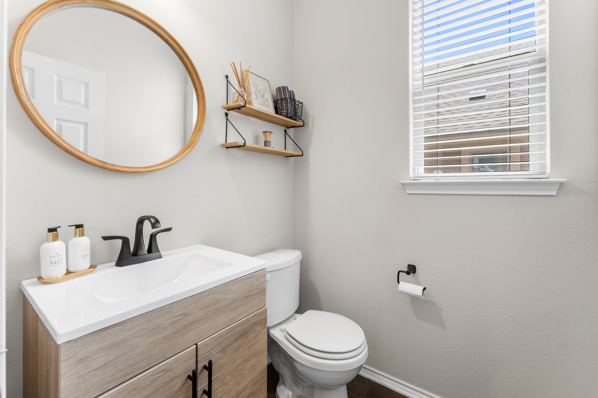 1133 Yellow Iris Road Leander, TX 78641 - Photo 15 of 37 Bathroom featuring a wood-finish vanity with an integrated sink, matte black faucet, and a round mirror