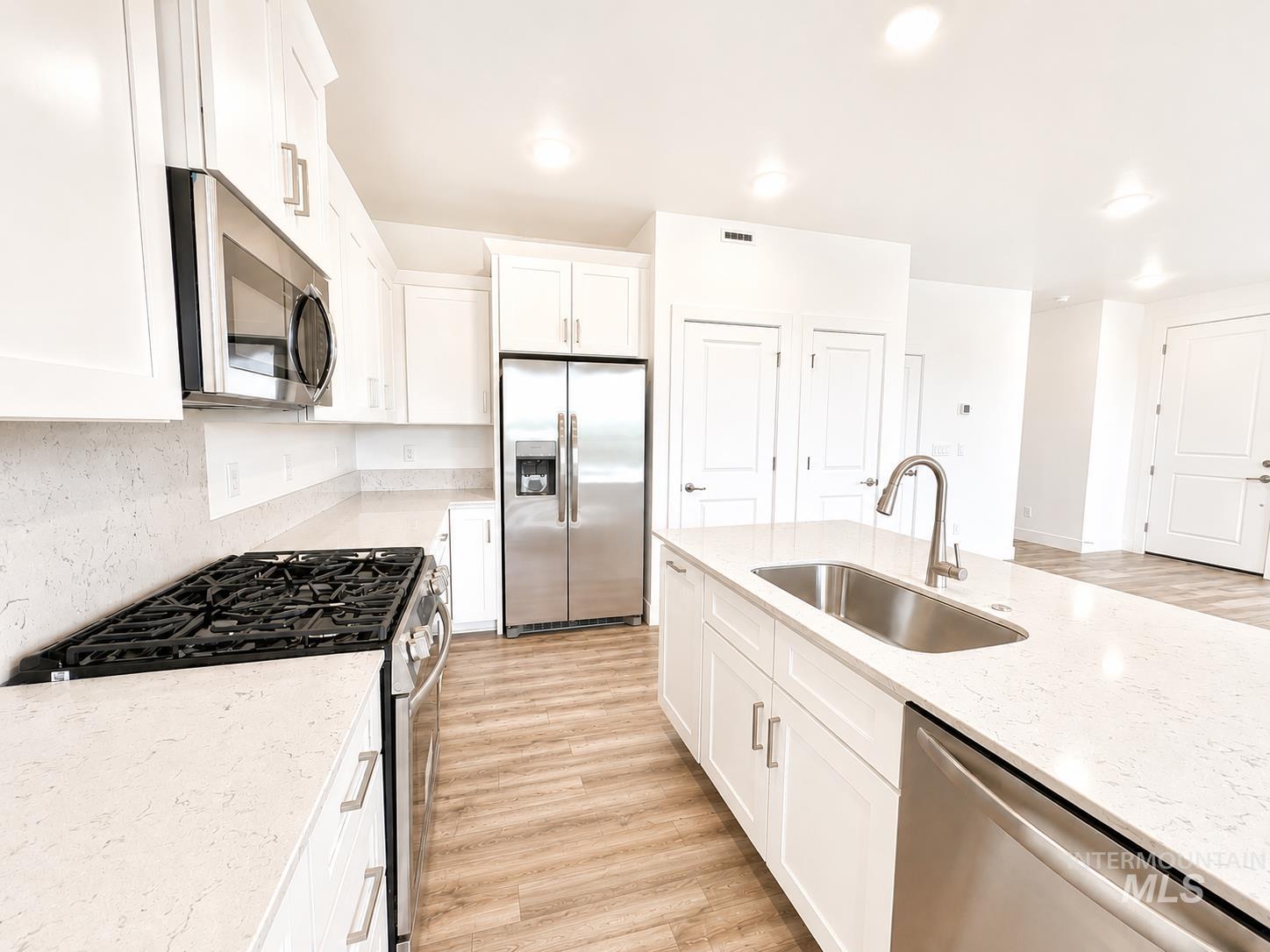 8098 West Fern Street Eagle, ID 83616 - Photo 5 of 22 Bright kitchen featuring white shaker cabinetry, stainless steel appliances, light-toned countertops, a gas range, and a kitchen island with an undermount sink