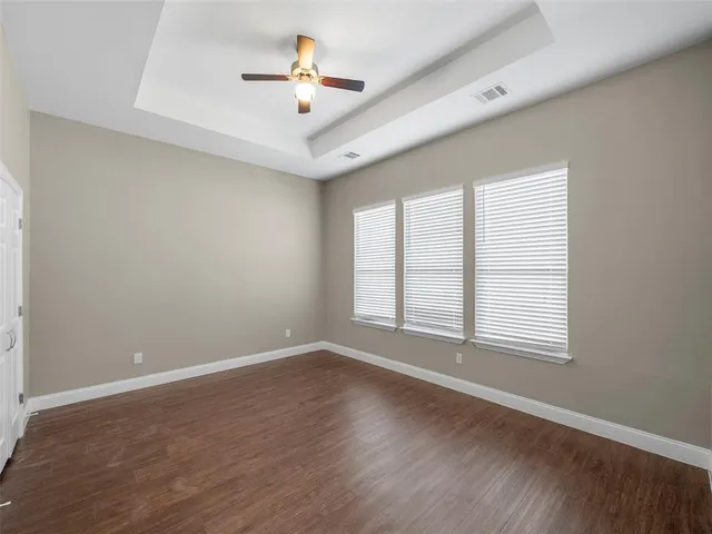 an empty room with wooden floor ceiling fan and windows