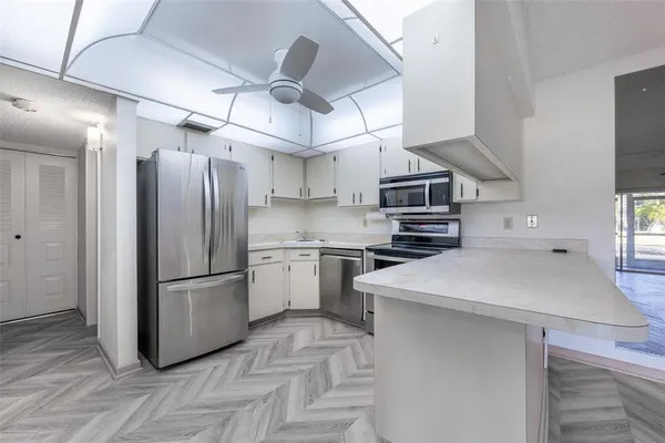 a kitchen with stainless steel appliances a refrigerator a sink dishwasher a stove and white cabinets with wooden floor