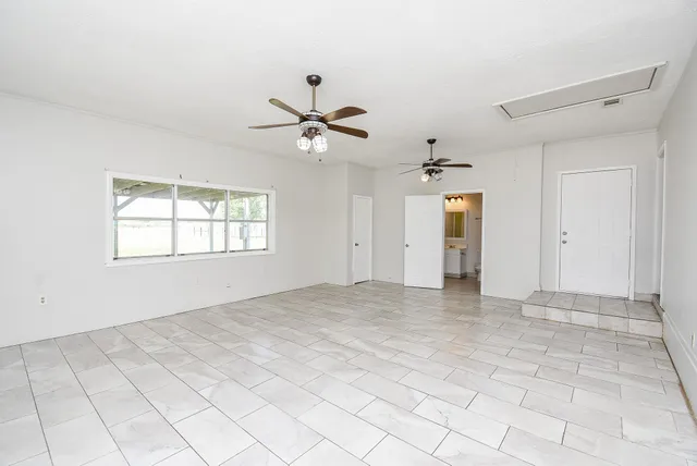 an empty room with chandelier fan and windows