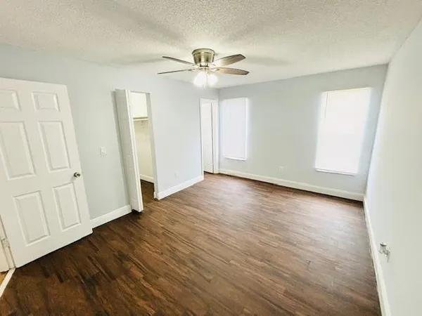 an empty room with wooden floor chandelier fan and windows