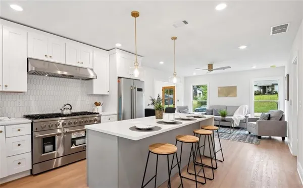 a kitchen with stainless steel appliances kitchen island granite countertop a stove a sink a refrigerator and chairs with wooden floor