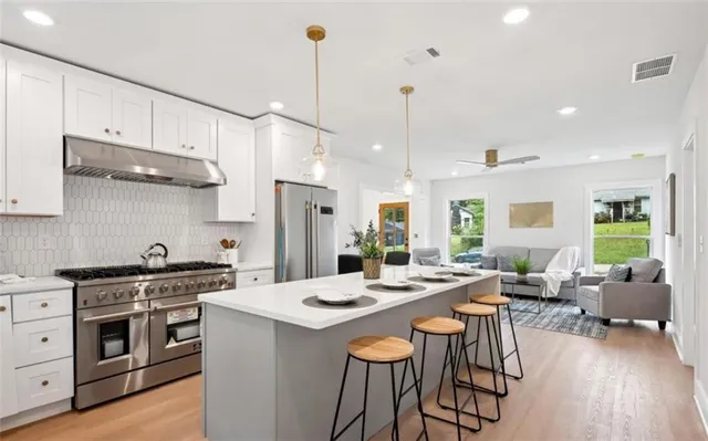 a kitchen with stainless steel appliances kitchen island granite countertop a stove a sink a refrigerator and chairs with wooden floor