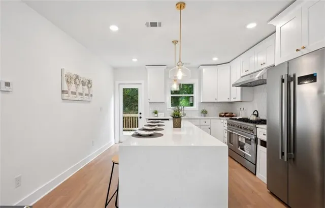 a kitchen with stainless steel appliances a refrigerator a stove a sink dishwasher a oven with white cabinets and wooden floor