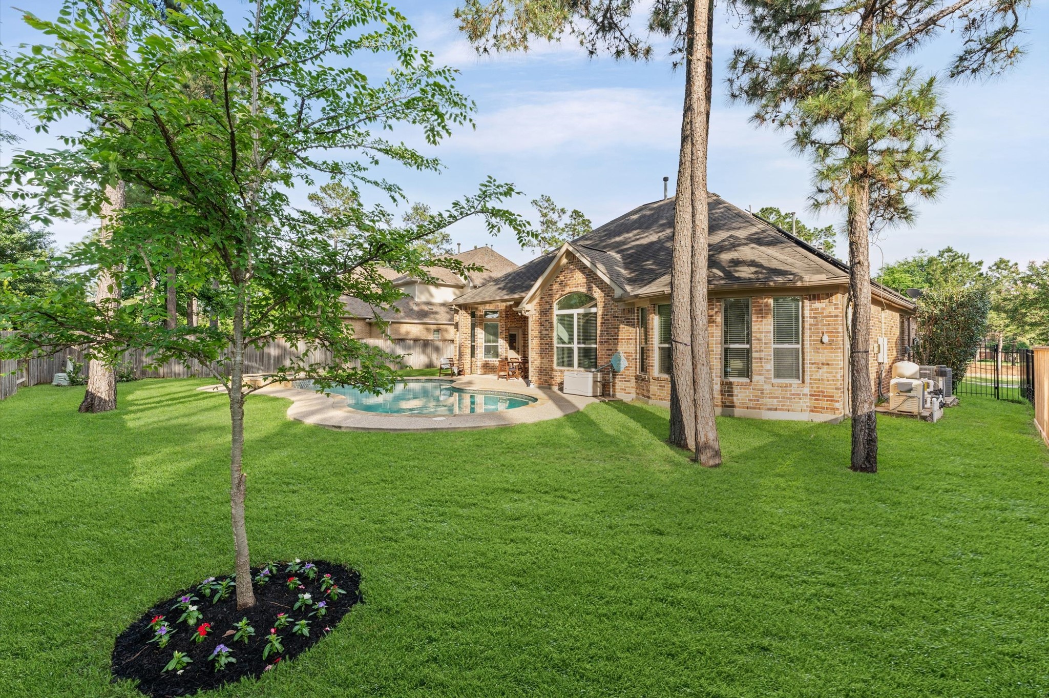 70 Valera Ridge Drive Spring, TX 77389 - Photo 4 of 37 This backyard features a spacious, well-maintained lawn with mature trees and a charming brick house. A curved swimming pool is centrally located, creating an inviting outdoor oasis perfect for relaxation and entertaining.