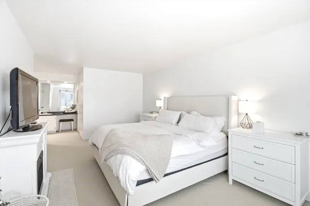 a bedroom with a bed a couch and a flat tv screen on the dresser