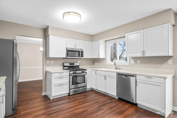 a kitchen with stainless steel appliances granite countertop a stove top oven a sink and white cabinets with wooden floor