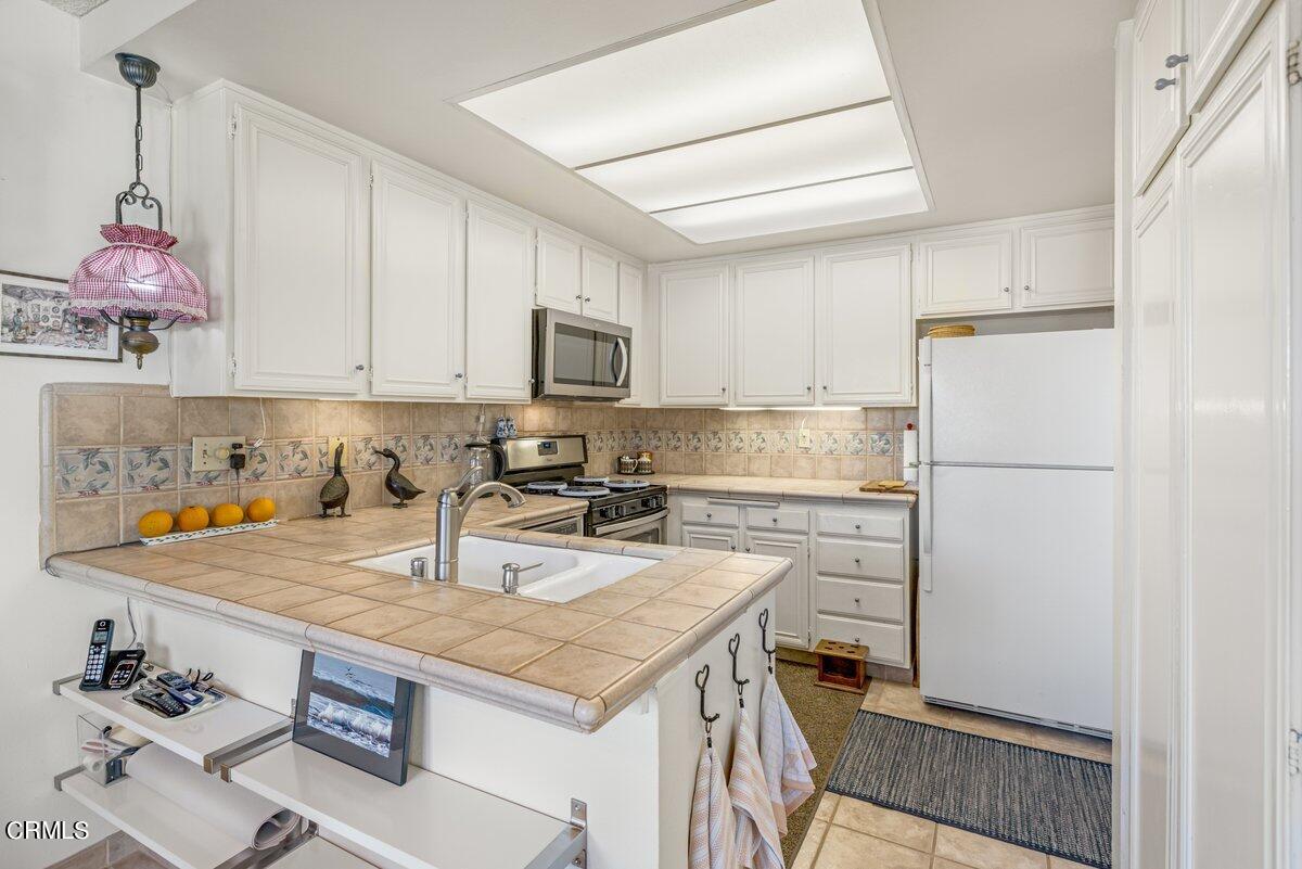 3330 Sunset Lane Oxnard, CA 93035 - Photo 13 of 29 a kitchen with granite countertop a refrigerator a stove a sink dishwasher and white cabinets with wooden floor