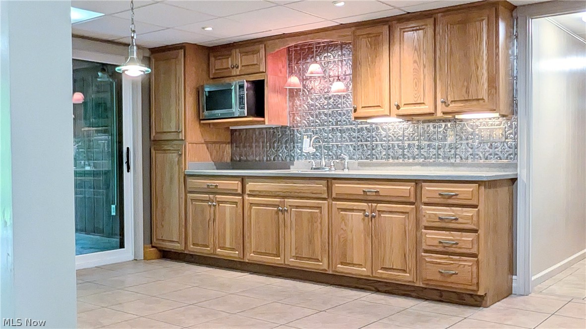 6409 Old Woods Road Ashtabula, OH 44004 - Photo 22 of 43 Built-in kitchenette featuring wood cabinetry, a microwave, composite countertops, a patterned tile backsplash, and a stainless steel sink