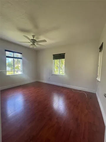 an empty room with wooden floor fan and windows