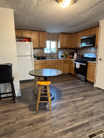 615 North 250 W Road Hinckley, UT 84635 - Photo 7 of 16 Kitchen featuring wood-finish flooring, natural wood cabinetry, a tiled backsplash, and stainless steel appliances