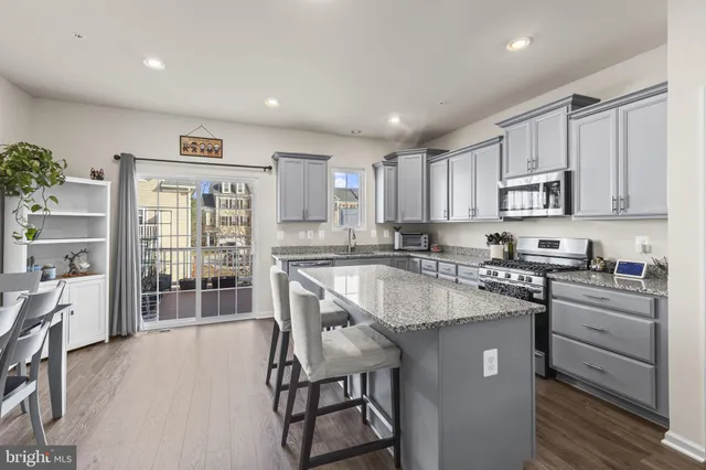 a kitchen with stainless steel appliances granite countertop a stove top oven a sink dishwasher a dining table and chairs with wooden floor