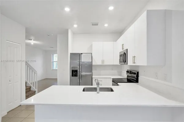 a kitchen with stainless steel appliances kitchen island granite countertop a refrigerator a sink a stove a microwave and white cabinets with wooden floor