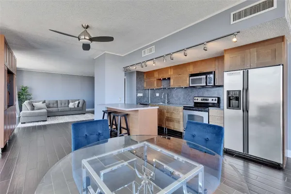 a kitchen with stainless steel appliances kitchen island granite countertop a refrigerator a stove a sink dishwasher a dining table and chairs with wooden floor