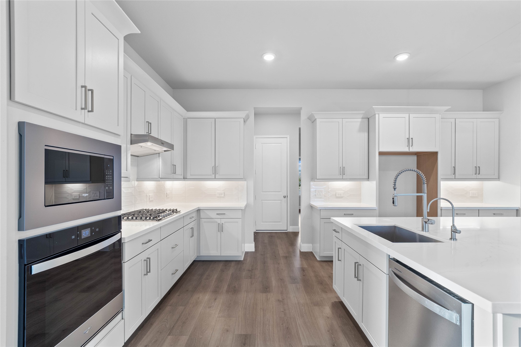 17020 Sweet Iris Court Conroe, TX 77302 - Photo 18 of 50 This gourmet kitchen is a study in modern elegance, featuring a cohesive design of crisp white Shaker-style cabinetry, sleek quartz countertops, and a seamless white subway tile backsplash. The chef-inspired space is fully equipped with high-end stainless steel appliances, including a built-in double oven and a gas cooktop, all anchored by a large central island with a deep undermount sink and industrial-style pull-down faucet.