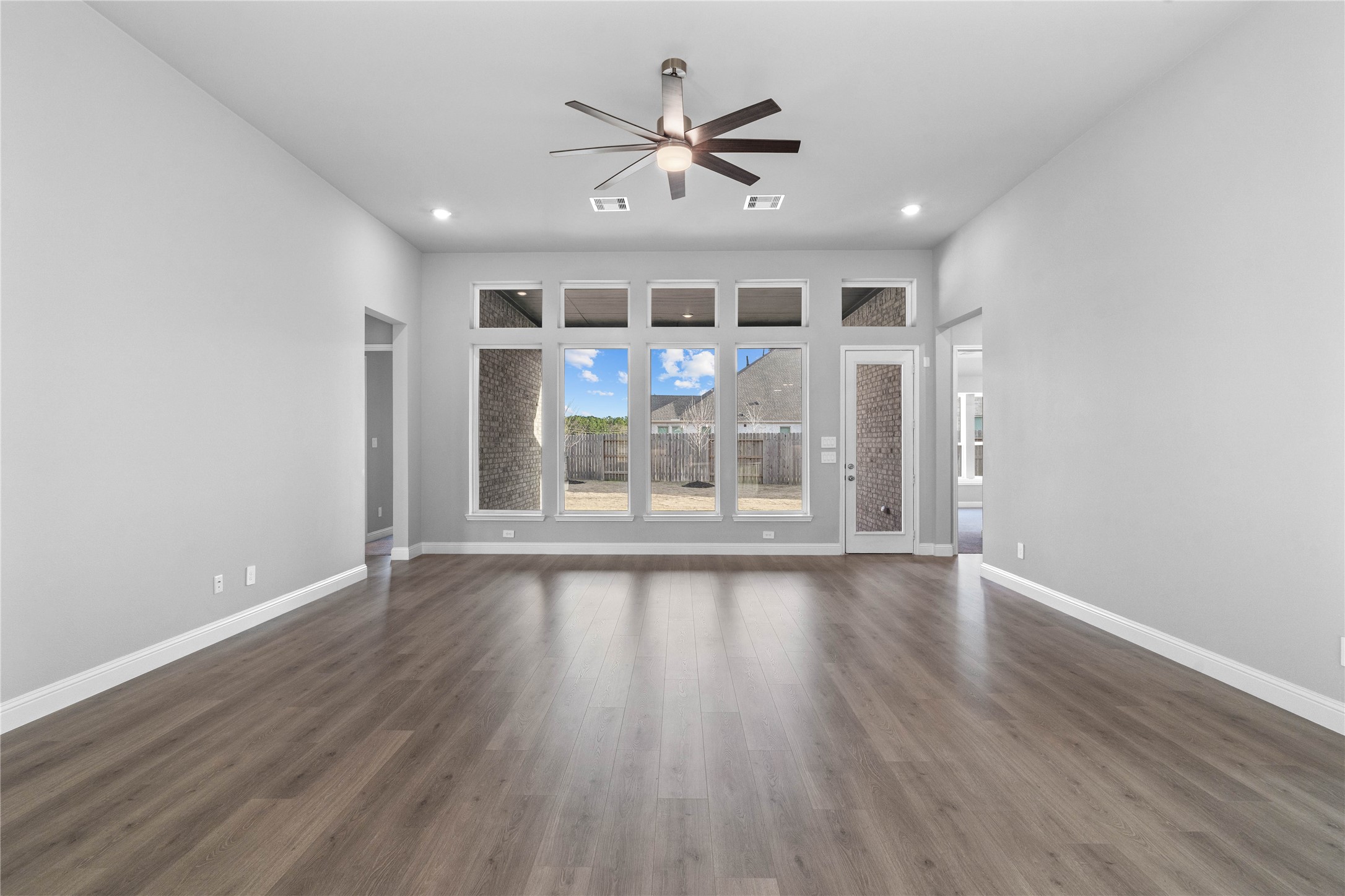 17020 Sweet Iris Court Conroe, TX 77302 - Photo 27 of 50 Enjoy the open and airy Family Room, designed for seamless entertaining and showcasing striking architectural details with high ceilings, recessed lighting, ceiling fan, durable laminate flooring, and a beautiful wall of windows that bring in an abundance of natural light and seamless flow to the covered rear patio.