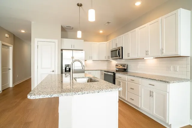 a kitchen with kitchen island granite countertop a stove top oven a sink a refrigerator and white cabinets with wooden floor