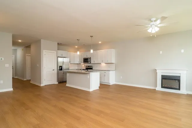 a view of kitchen with kitchen island a sink dishwasher a refrigerator and white cabinets with wooden floor