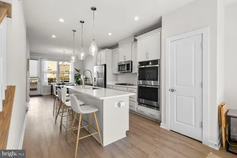 a kitchen with stainless steel appliances kitchen island granite countertop a refrigerator oven a sink dishwasher and white cabinets with wooden floor