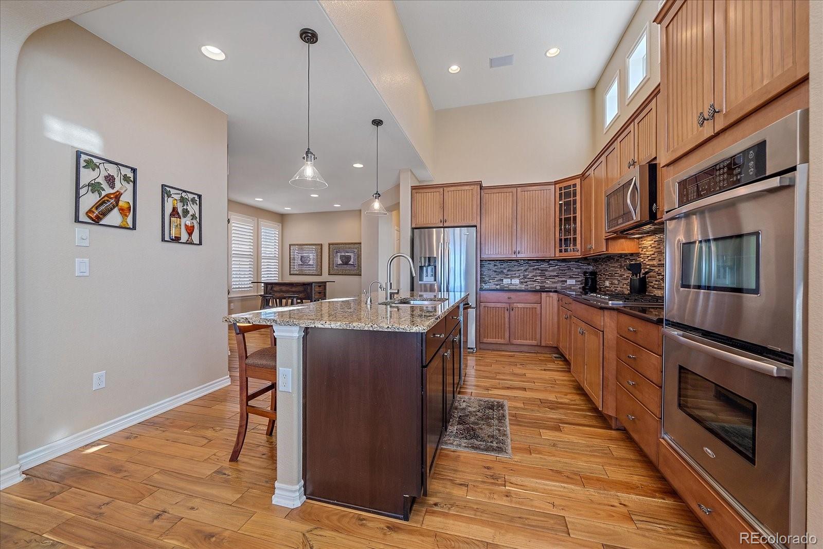 9317 Viaggio Way Highlands Ranch, CO 80126 - Photo 9 of 50 a large kitchen with stainless steel appliances kitchen island granite countertop a refrigerator a stove a sink a dining table and chairs with wooden floor