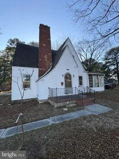 a view of a white house next to a yard with large trees