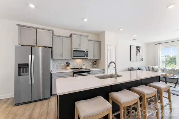 a kitchen with stainless steel appliances a sink stove refrigerator and white cabinets with wooden floor