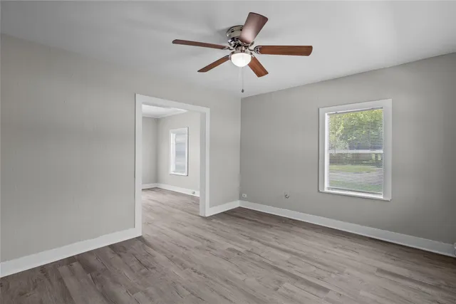 an empty room with wooden floor ceiling fan and windows