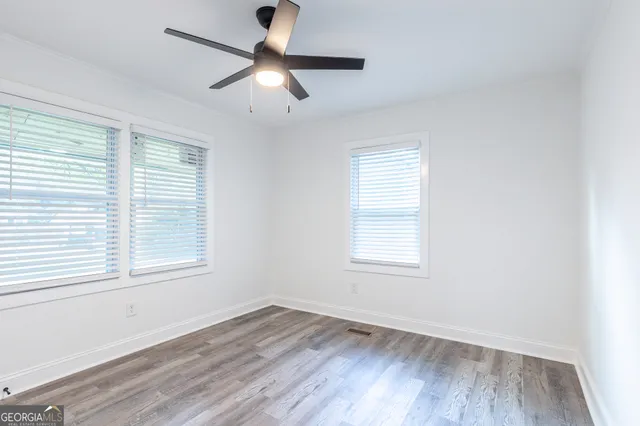 an empty room with wooden floor ceiling fan and windows