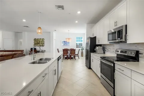 a kitchen with stainless steel appliances a sink a stove top oven a chimney a dining table and chairs